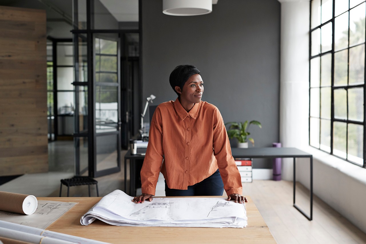 Femme debout devant un bureau réfléchissant à des plans sur mesure sur papier