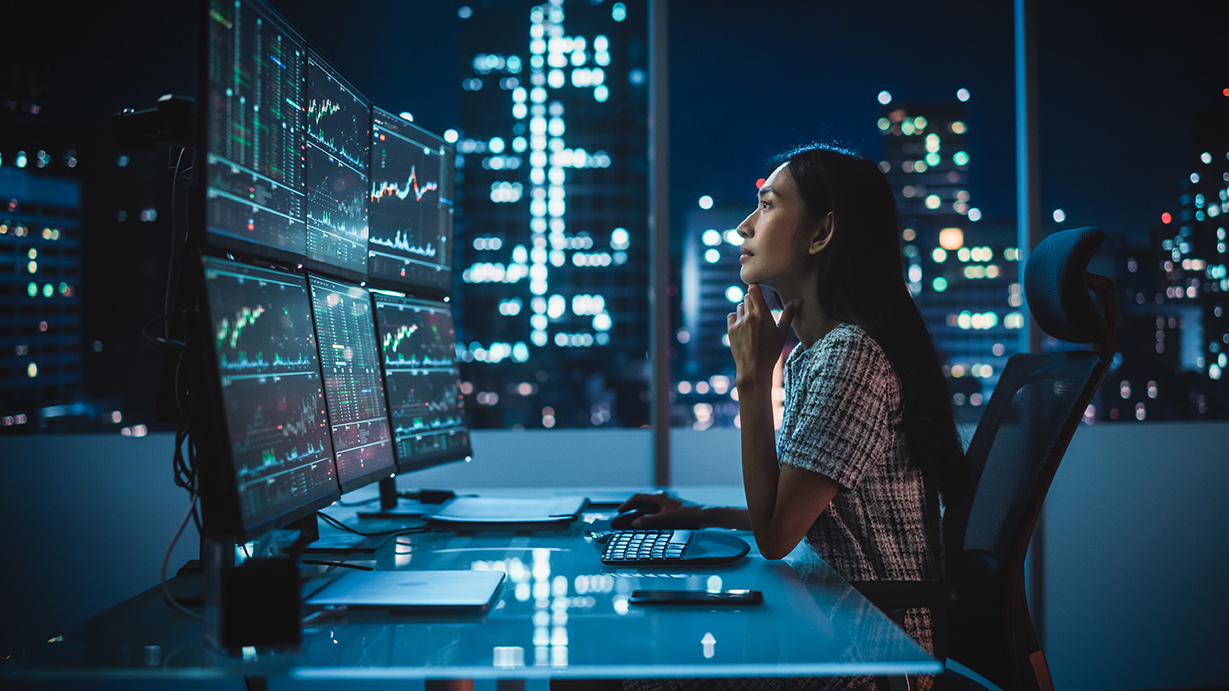 Woman in an office looking at her computer that is showing graphics at night